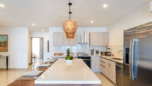 Une cuisine moderne dotée d’un îlot central, d’appareils électroménagers en acier inoxydable et d’un luminaire suspendu original.