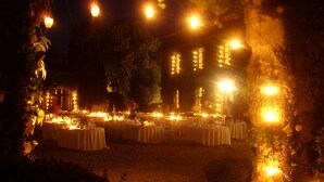 Zona d'esbarjo a l'aire lliure amb taules preparades per a dinar, envoltada d'arbres i il·luminada amb llums de garlandes.