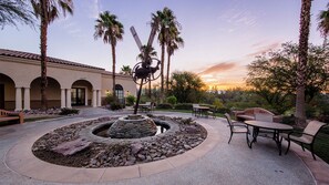 A courtyard with a stone fountain, outdoor seating, palm trees, and a building with arches. - Spacious 1BR Villa at Marriott's Shadow Ridge – Full Kitchen + Golf Resort (Palm Desert)