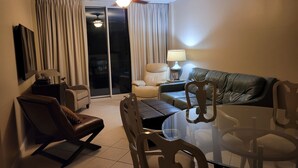 A hotel room with a glass dining table, leather sofas, a ceiling fan, and a sliding glass door leading to an outdoor area.