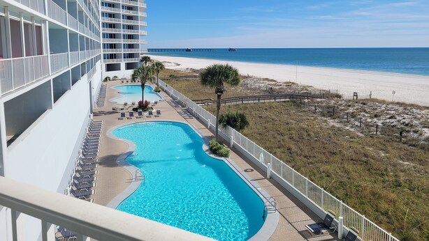 A hotel with a pool, beach view, and a pier in the distance.