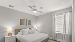 Un dormitorio con una cama, mesitas de noche, un ventilador de techo y una ventana con cortinas.