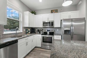 Una cocina moderna con armarios blancos, electrodomésticos de acero inoxidable y encimera de granito.