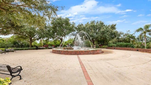 Un espace circulaire aménagé en parc, avec une fontaine centrale, entouré de bancs et d’arbres.