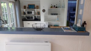 A kitchen with a microwave, a white cabinet, a shelf with kitchen items, and a window with curtains. - Studio Avec Jardin au Bord de la Rivière Avec Jacuzzi (Annot)