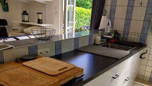 A modern kitchen with a black countertop, white cabinets, and a window providing a view of greenery outside. - Studio Avec Jardin au Bord de la Rivière Avec Jacuzzi (Annot)