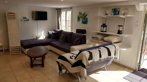A living room with a sectional sofa, a round coffee table, a small side table, a TV mounted on the wall, and a window with curtains. - Studio Avec Jardin au Bord de la Rivière Avec Jacuzzi (Annot)