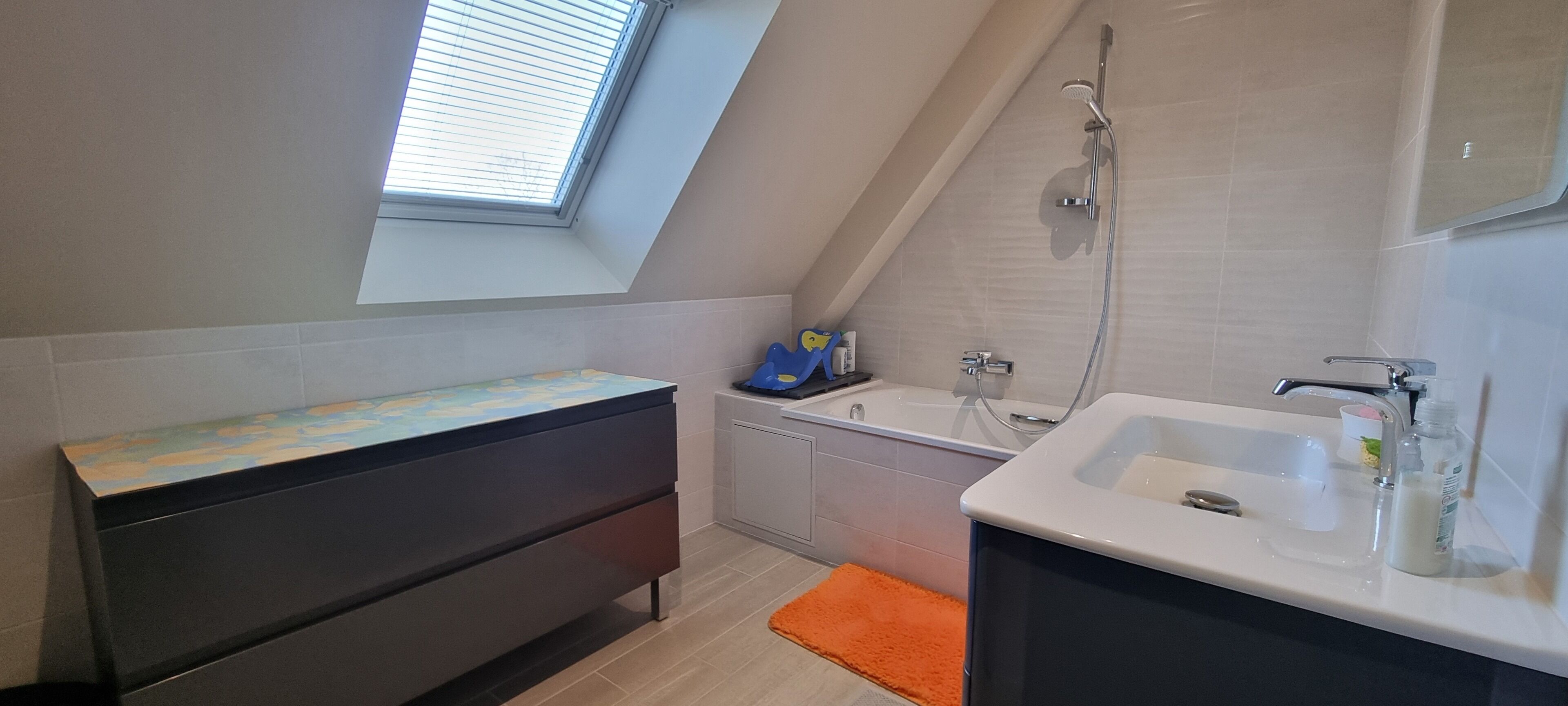 Un bagno moderno con finestra sul tetto, una vasca, un mobile lavabo e un tappeto arancione.