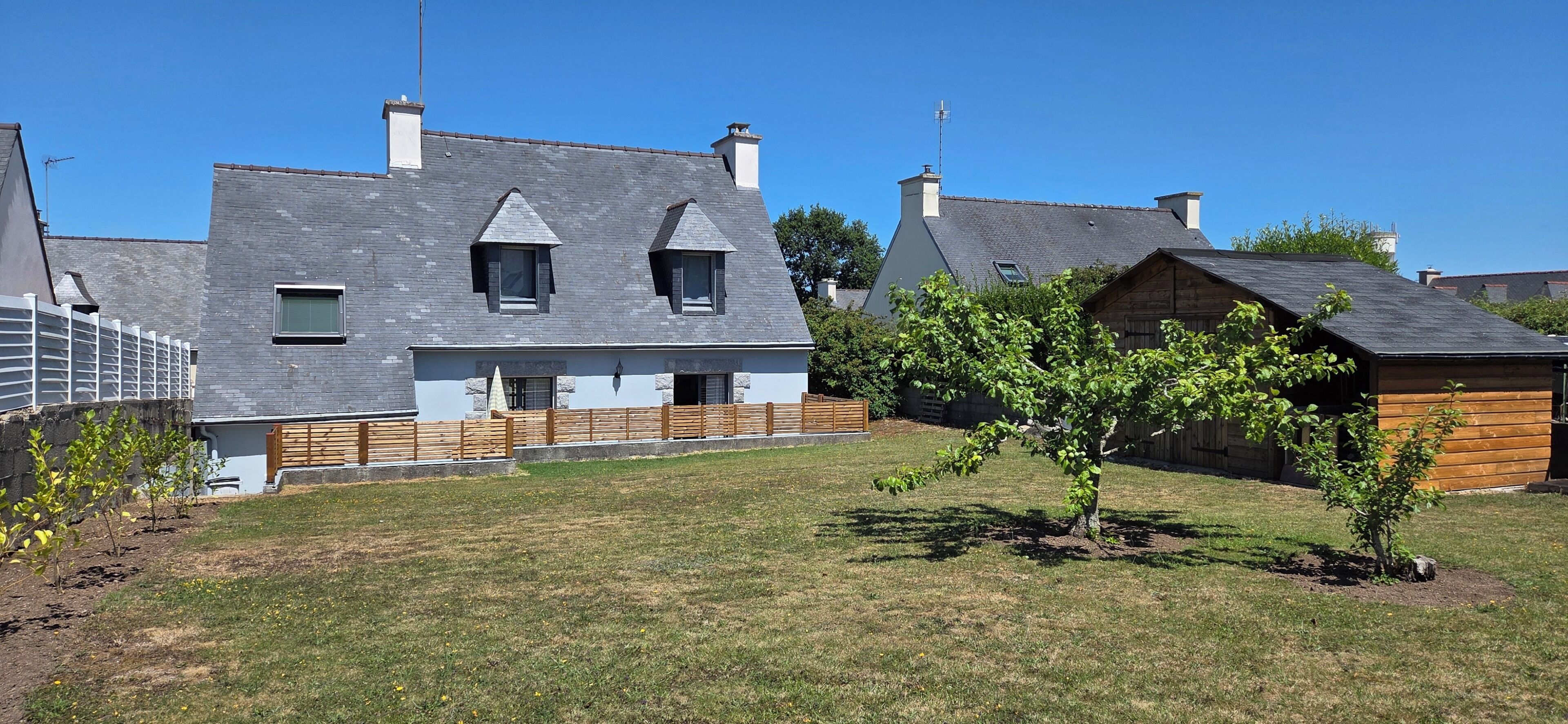 Il s’agit d’une propriété résidentielle comprenant une maison grise, une clôture en bois et un petit arbre.