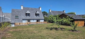 A residential property with a grey house, a wooden fence, and a small tree. - Belle Maison Lumineuse Avec Jardin Clos au Centre de Nevez - 500m des Commerces (Névez)