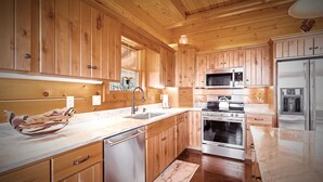 A kitchen with wooden cabinets, stainless steel appliances, and a marble countertop. - Outstanding Views! 5BR/4.5 BA/ Sleeps 14, Hot-Tub, Pool Table! (Maggie Valley)