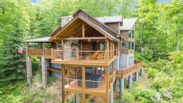 A multi-level wooden cabin with a balcony and outdoor seating area, surrounded by dense forest. - Outstanding Views! 5BR/4.5 BA/ Sleeps 14, Hot-Tub, Pool Table! (Maggie Valley)