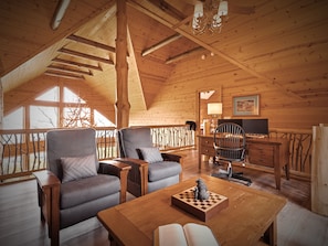 A cozy wooden interior with a loft-style ceiling, a wooden desk, two armchairs, and a chessboard. - Outstanding Views! 5BR/4.5 BA/ Sleeps 14, Hot-Tub, Pool Table! (Maggie Valley)