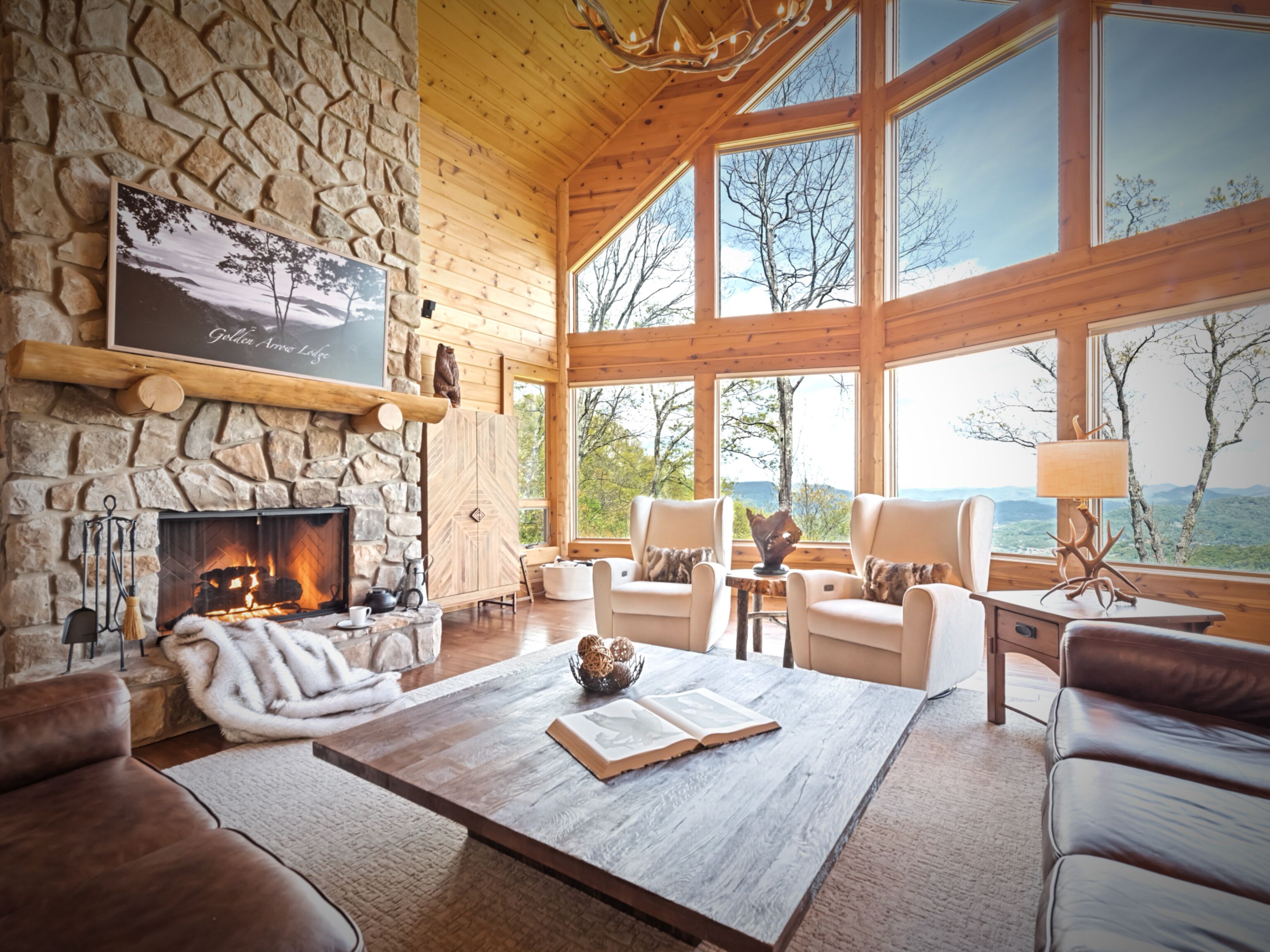A cozy room with a stone fireplace, wooden walls, and large windows offering a view of the outdoors.