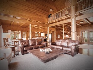 A spacious living area with a large brown leather sofa, a wooden coffee table, and a dining table with chairs.