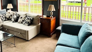 A living room with a sofa set, a coffee table, and a lamp. There are windows with a view of a fenced yard. - Pet Friendly - 6 Guests - Haven Lakeland (Grange-over-Sands)