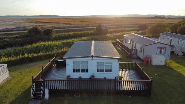 A white mobile home with a deck, surrounded by grassy fields and a distant view of hills. - Pet Friendly - 6 Guests - Haven Lakeland (Grange-over-Sands)