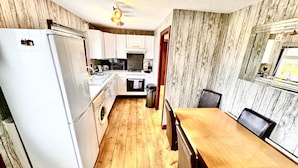 A compact kitchen with a refrigerator, oven, microwave, and sink. There is a wooden dining table with chairs and a small window with a view. - Pet Friendly - 6 Guests - Haven Lakeland (Grange-over-Sands)