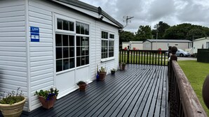 A white building with a blue sign, a wooden deck, and potted plants. - Pet Friendly - 6 Guests - Haven Lakeland (Grange-over-Sands)