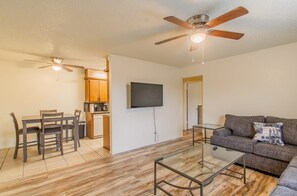 A modern living room with a glass coffee table, a sofa, a dining area with chairs, a kitchen with wooden cabinets, and a ceiling fan. - A bedroom in close proximity to Fort Sill! (Lawton)