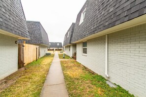 A narrow pathway between two brick buildings with a wooden fence on one side. - A bedroom in close proximity to Fort Sill! (Lawton)
