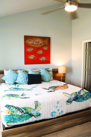 Een slaapkamer met een bed, kussens, een kunstwerk van vissen, een lamp en een plafondventilator.