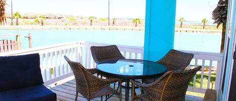 A covered outdoor area with a table and chairs, a sofa, and a view of a body of water and distant landscape.