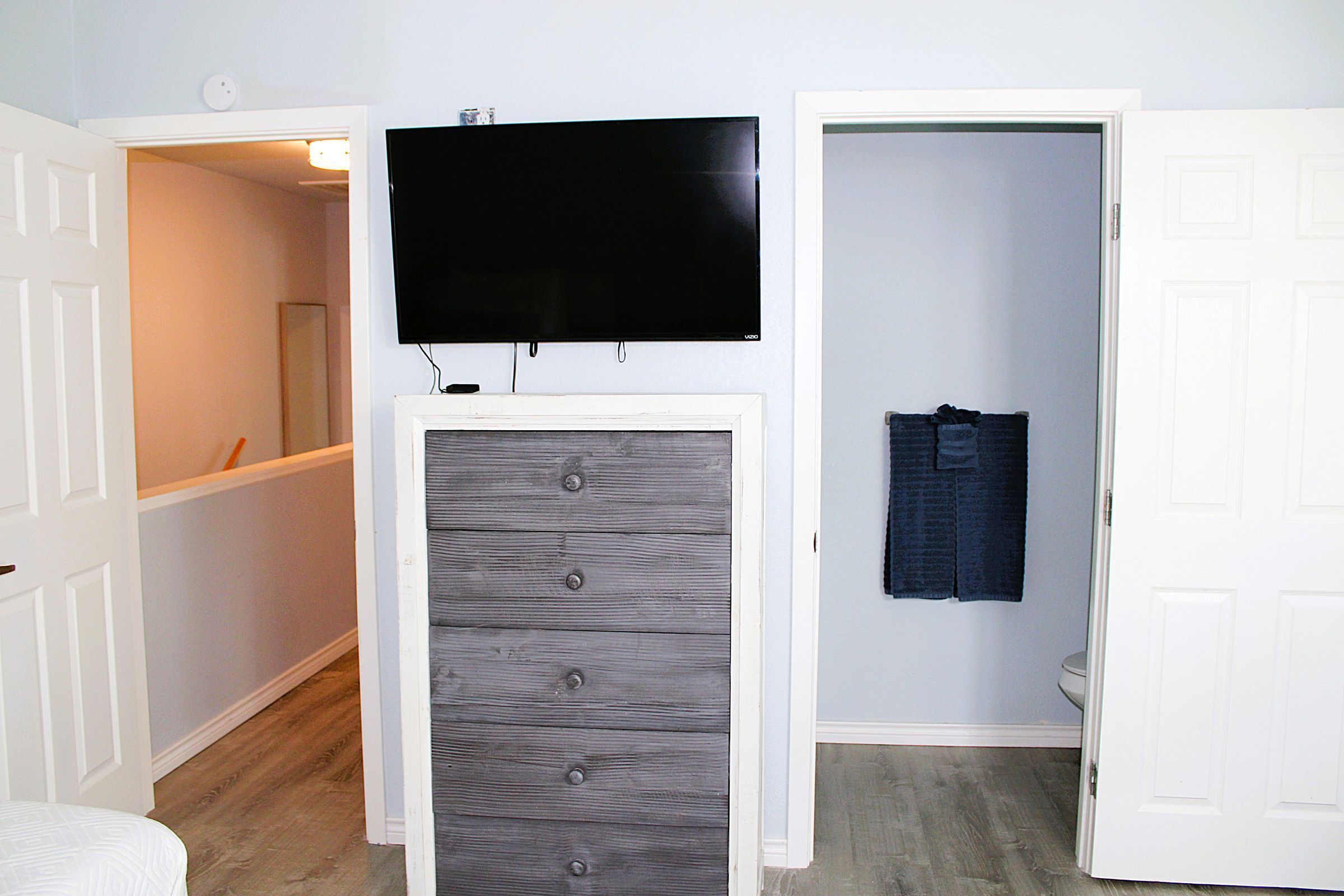 A room with a television mounted on the wall, a wooden cabinet, and a closet with a towel hanging.