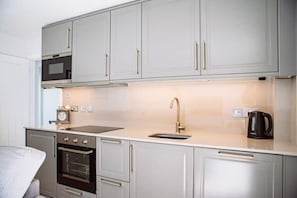 Een moderne keuken met grijze kastjes, een roestvrijstalen oven, een magnetron, een gouden kraan en een zwarte koffiezetapparaat.