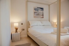 Een slaapkamer met een bed, nachtlampjes, een schilderij en een nachtkastje met een vaas.