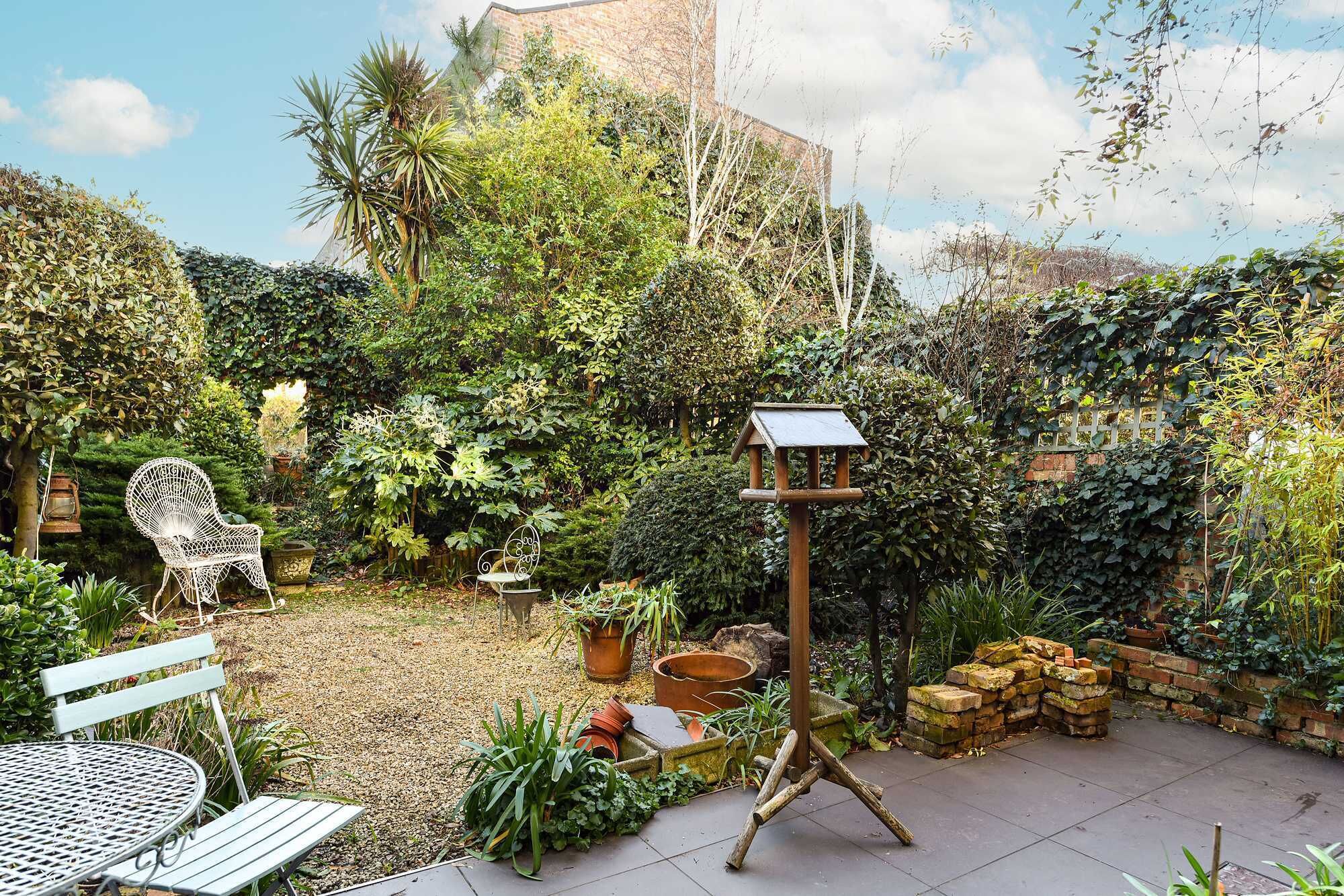 Un jardin avec une table en métal, des chaises et une mangeoire à oiseaux.