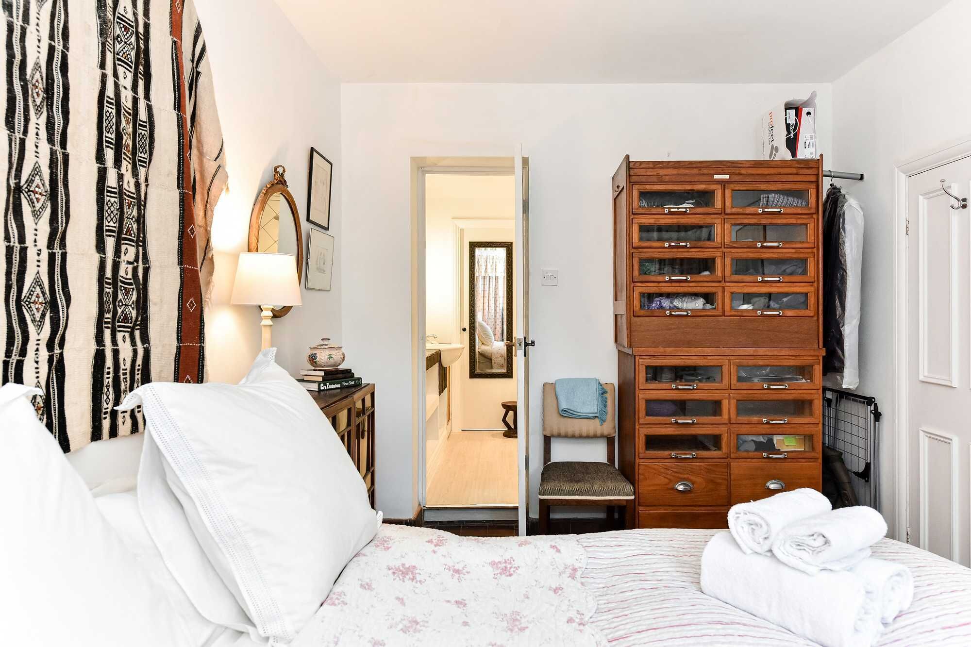 A bedroom with a bed, a wooden dresser with multiple drawers, a chair, and a mirror.