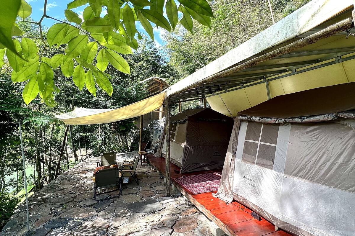 Un terrain de camping avec une tente, une table et une chaise sous un auvent.
