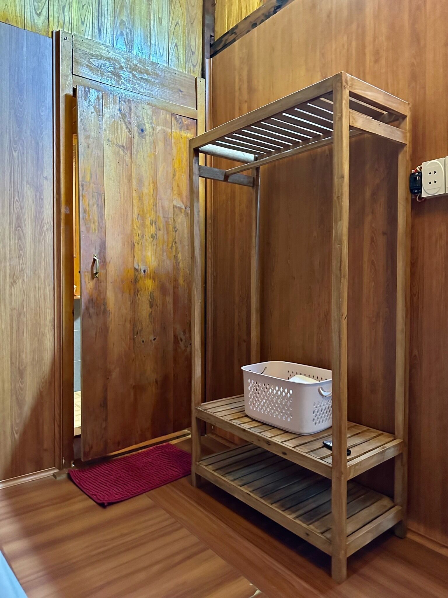 Una mensola in legno con un cesto sullo scaffale inferiore, una porta con maniglia e una presa elettrica sulla parete.