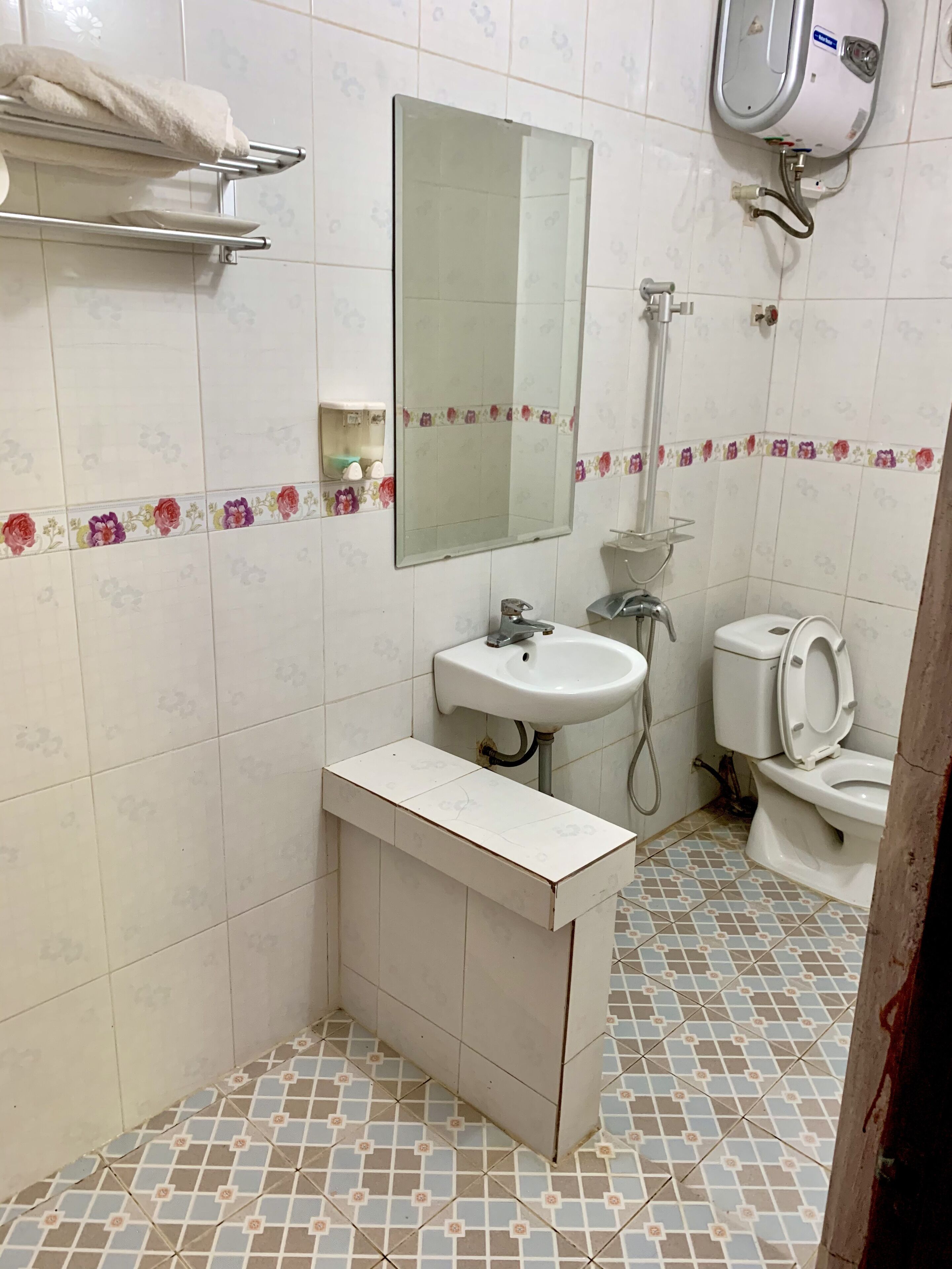 Et badeværelse med håndvask, spejl, toilet og en håndtørrer.