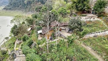 Una cabaña rústica con un sendero de piedra que conduce a ella, rodeada de abundante vegetación y un río al fondo.