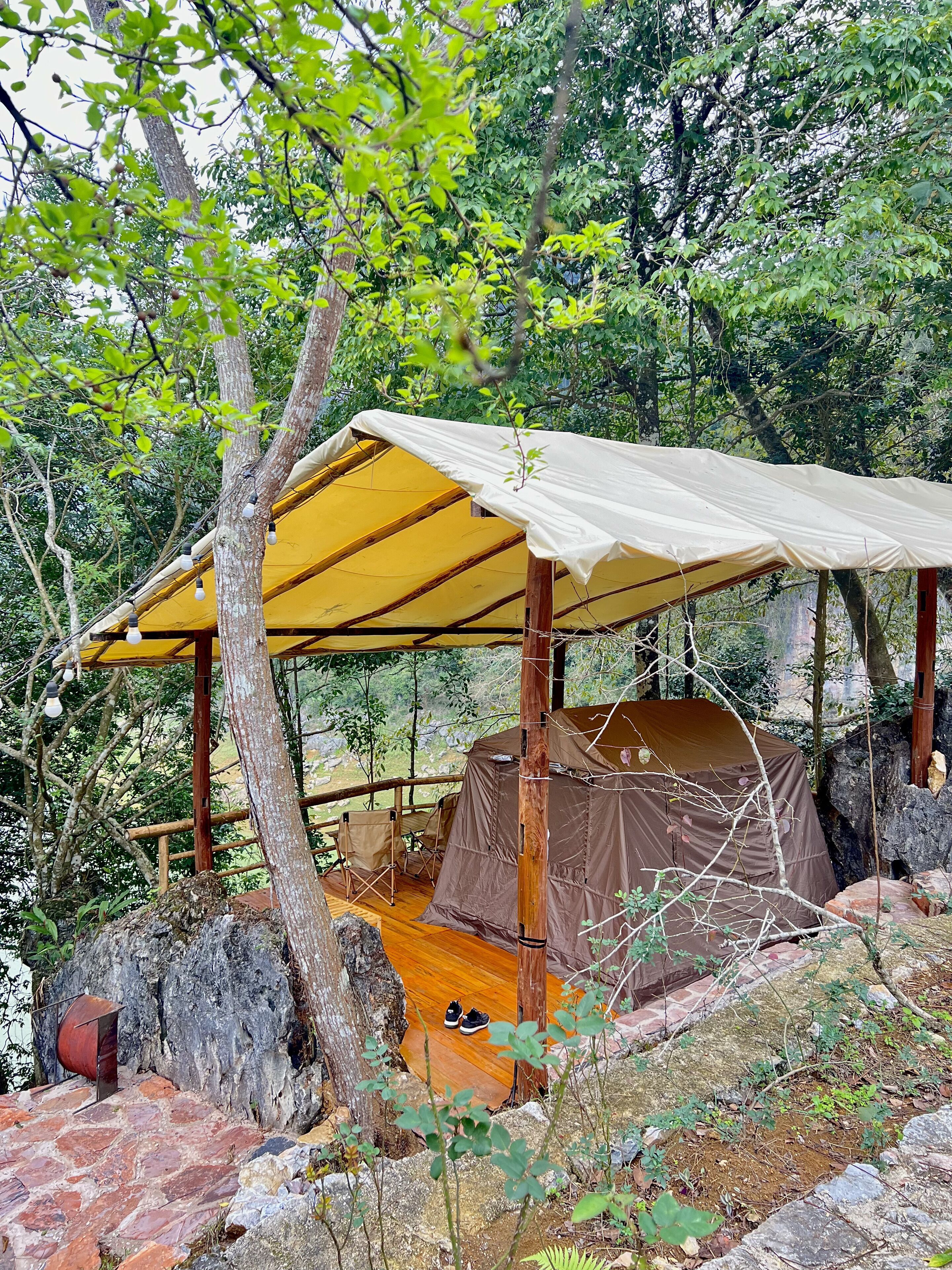 A tent with a wooden floor and a canopy, surrounded by trees and rocks.