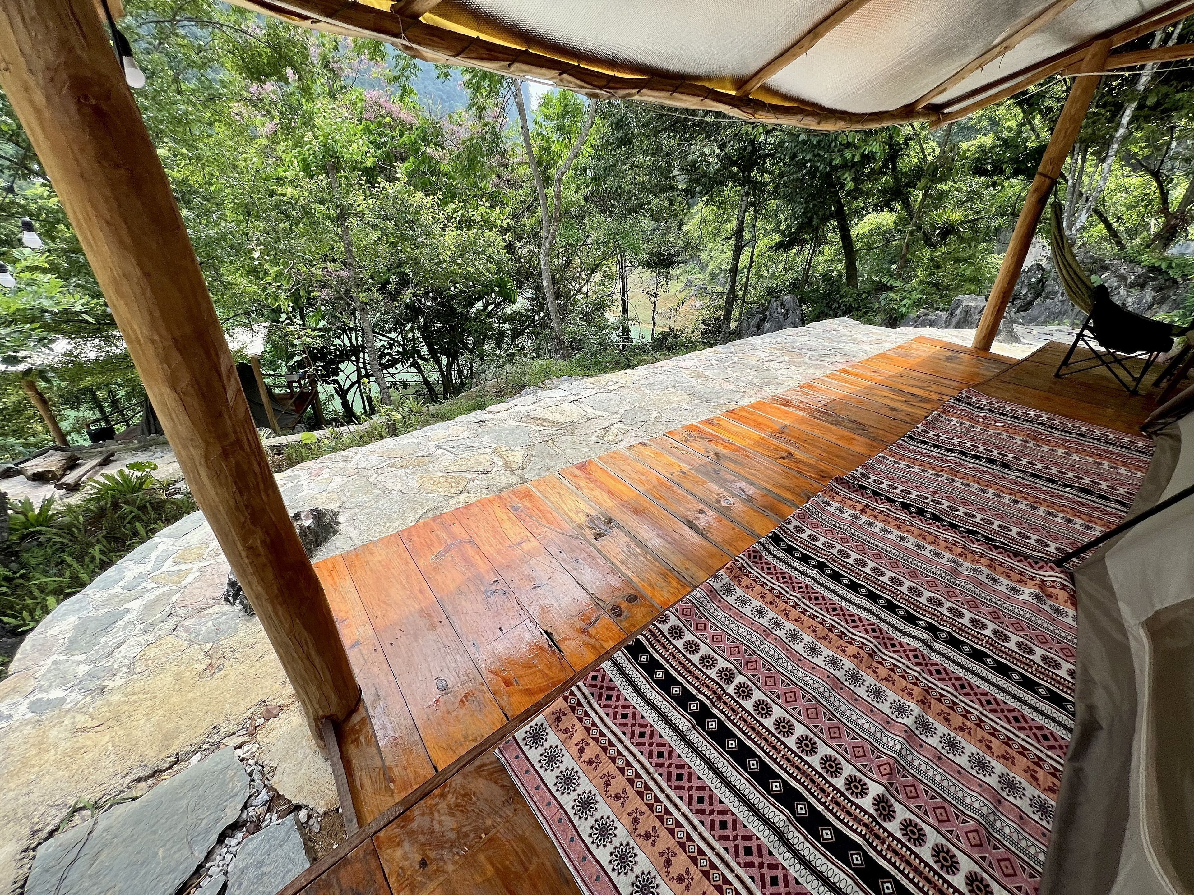 A wooden deck with a patterned rug, surrounded by stone walls and lush greenery.