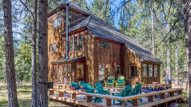 Une cabane en bois dotée d’une terrasse, de nombreuses fenêtres et d’un espace salon extérieur.
