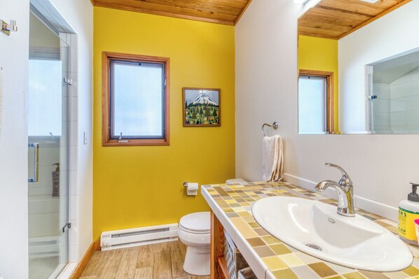 Une salle de bain avec un mur jaune, des toilettes blanches, un lavabo avec un plan de travail à carreaux et une fenêtre donnant sur un paysage de montagne.