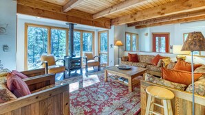 Un intérieur chaleureux avec un plafond en bois, de grandes fenêtres, une cheminée et un canapé agrémenté de coussins à motifs.