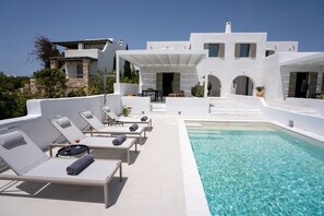 Eine moderne, weiße Villa mit Pool, Liegestühlen und einer überdachten Terrasse.