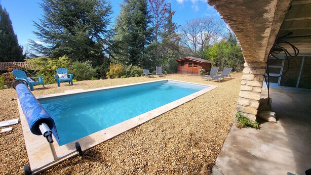 A rectangular swimming pool with a pebble surround, surrounded by blue chairs and a small wooden building. - Au Centre du Village, Maison Avec Beau Jardin Arboré , Piscine Chauffée (Saint-Saturnin-lès-Apt)