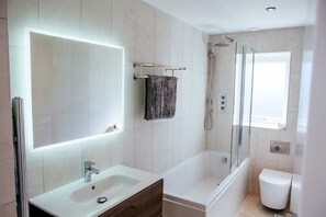 Een moderne badkamer met een grote spiegel, een wastafel, een bad en een douche.