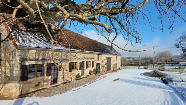 A stone building with a snow-covered ground, a paved path, and a fenced area. - La Maison de Barbara (La Guiche)
