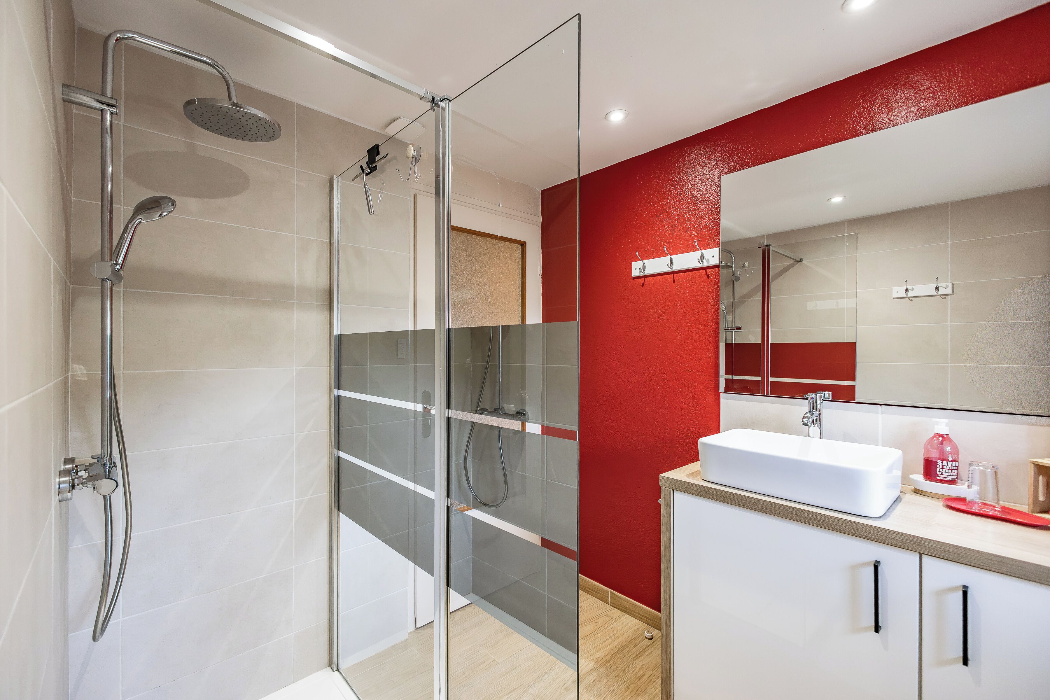Un baño moderno con cabina de ducha de vidrio, un lavabo blanco y una pared de acento roja.