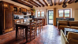 A rustic kitchen with wooden cabinets, a dining table, and chairs. There is a window with a view of the outdoors. - La Maison de Barbara (La Guiche)