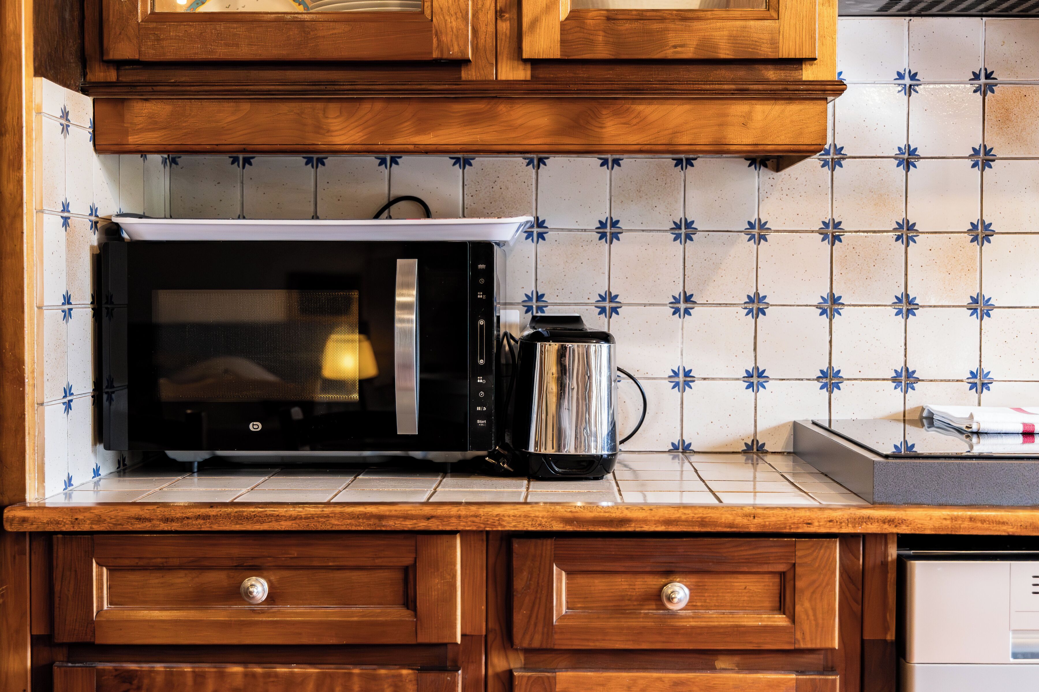 A kitchen with a microwave, coffee maker, wooden cabinets, and a tiled backsplash.