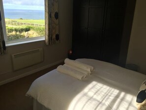 Een kamer met een bed, een raam met uitzicht op zee en een deur.