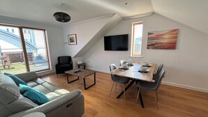 Ein modernes Wohnzimmer mit Essbereich, großen Fenstern, einem Flachbildfernseher und einem Bild an der Wand.